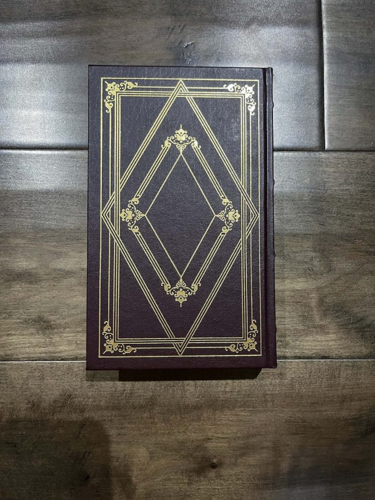 image of the side of David Copperfield book. It is a purplish brown with gold rectangle and two diamonds in the center like a 1920's aesthetic