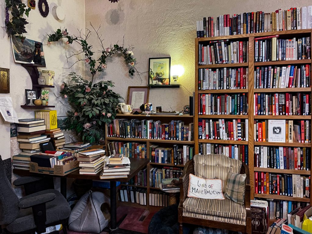 A section after the hallway in where a rocking chair is placed in front of a lot of bookcases and to the right of a desk stacked with books