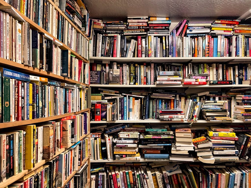 left corner of books on shelves from the floor to the ceiling with stacks of books in front of those and stacks of books on the floor