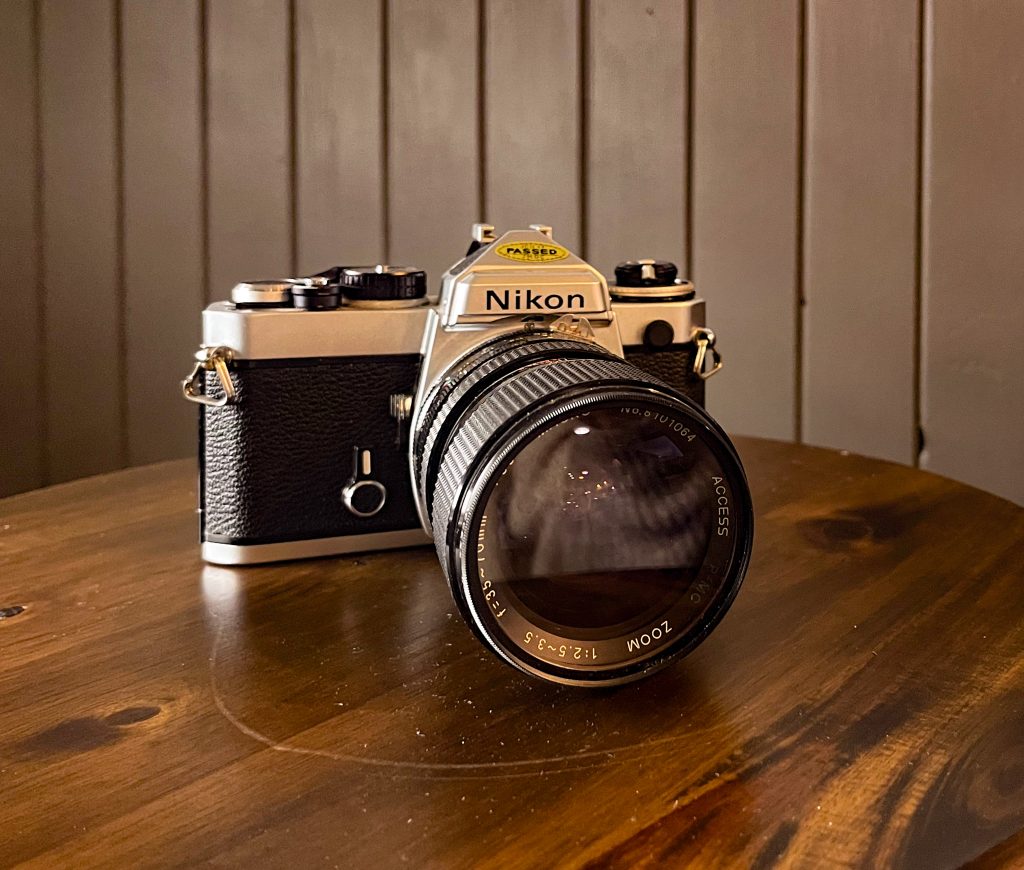 Nikon film camera without a lens sitting on stand in front of brown wall